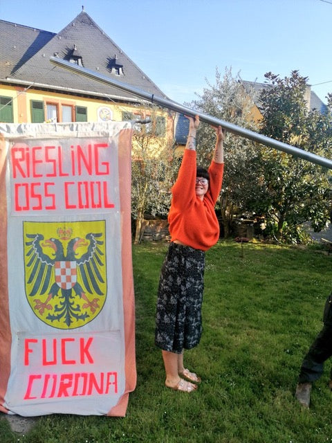 Jas Swan of Katla Wines holds a flag that says "Riesling Oss Cool" "Fuck Corona"